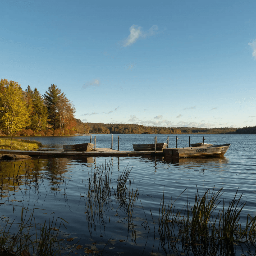 A serene lake scene featuring two boats at a wooden dock surrounded by autumn foliage.