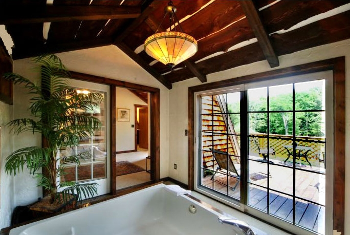 The Loft whirlpool salon with a large jetted tub and a sliding glass door that opens onto an outdoor deck and greenery.