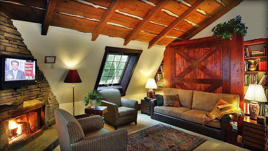 A cozy, rustic loft living room featuring a stone fireplace, exposed wood beams, and a comfortable sofa and armchairs.