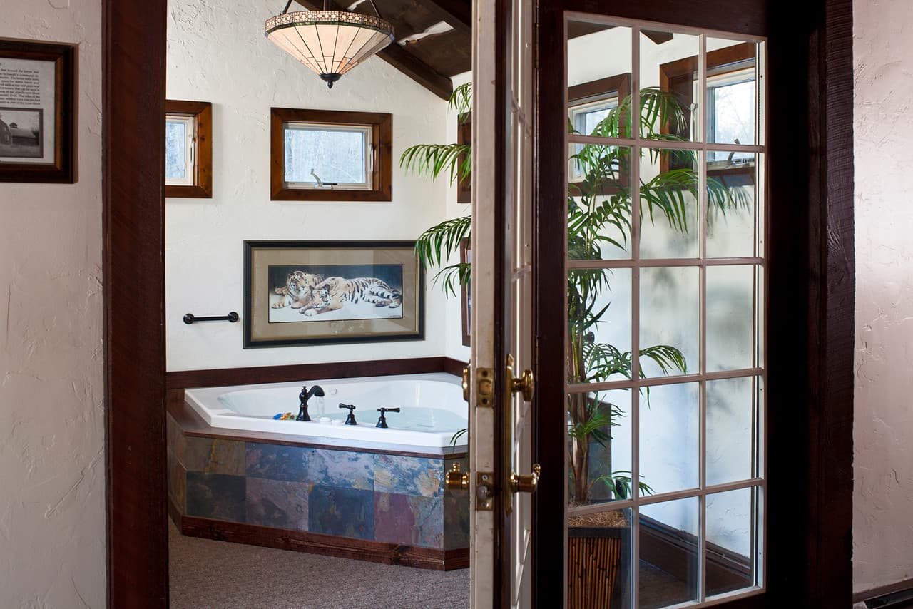 View of the Loft whirlpool salon with a tiled jetted tub and a plant, seen through open French doors with frosted glass.