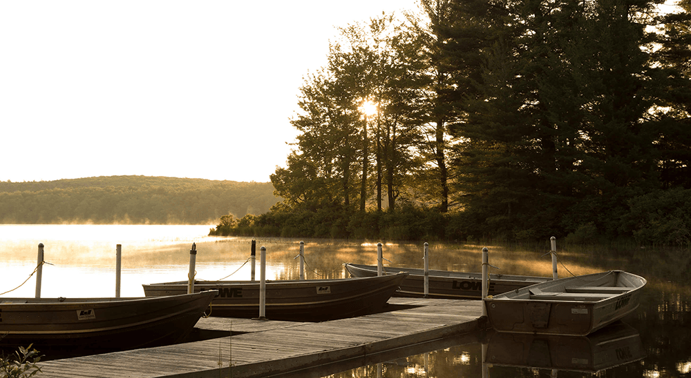 A tranquil lake at sunrise with boats docked on a wooden pier surrounded by trees.