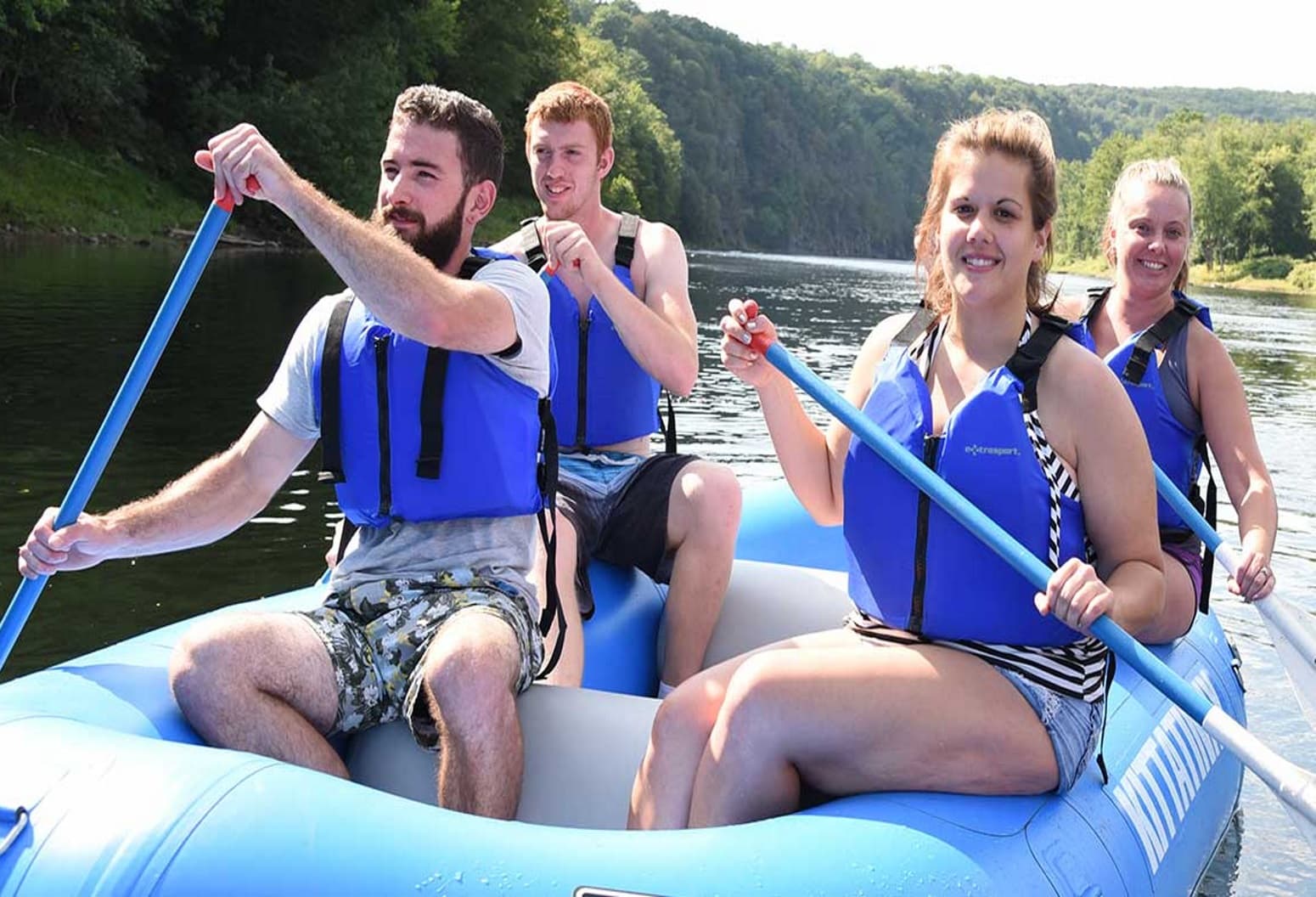 A group of four people paddling together in a blue raft on a river. A group of four people paddling together in a blue raft on a river.