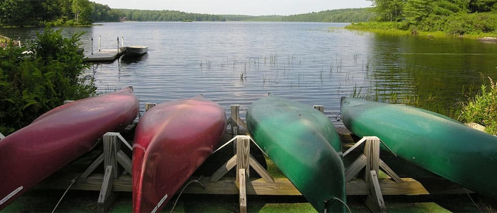 Four canoes in red and green lined up on docks beside a serene lake.