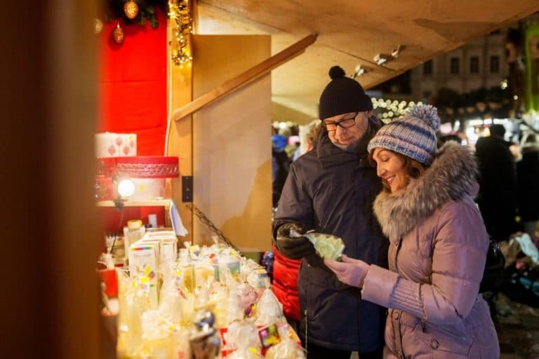 A man and woman smile while examining festive items at a holiday market.