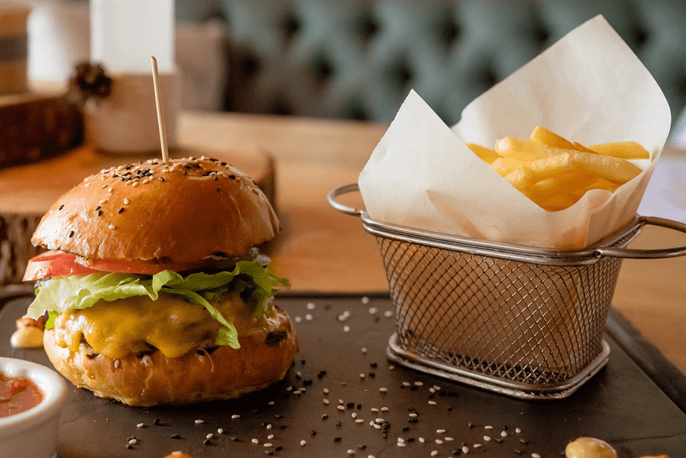 A cheeseburger with lettuce and tomato beside a small basket of fries.