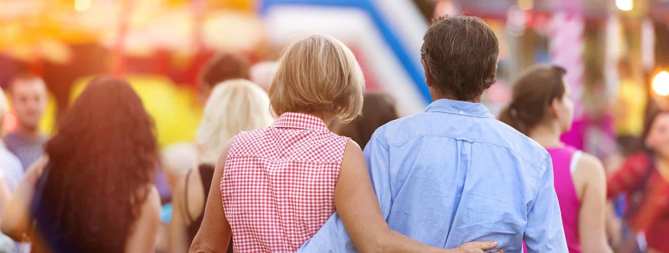 A couple walks together, embracing, amidst a crowd at a festive event.