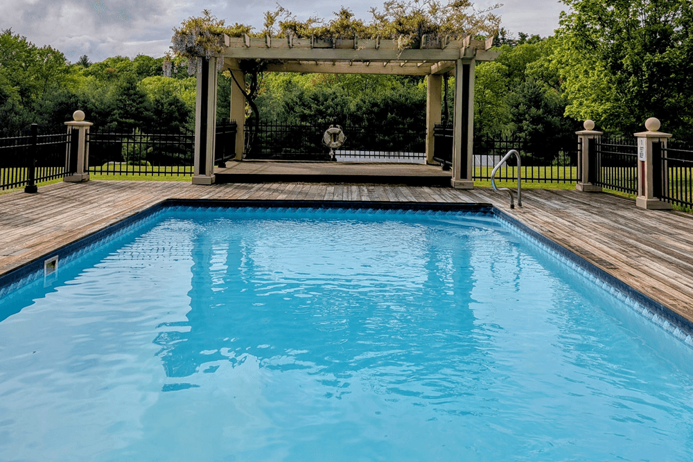A sparkling blue pool in a serene outdoor setting with a wooden deck and a pergola in the background.