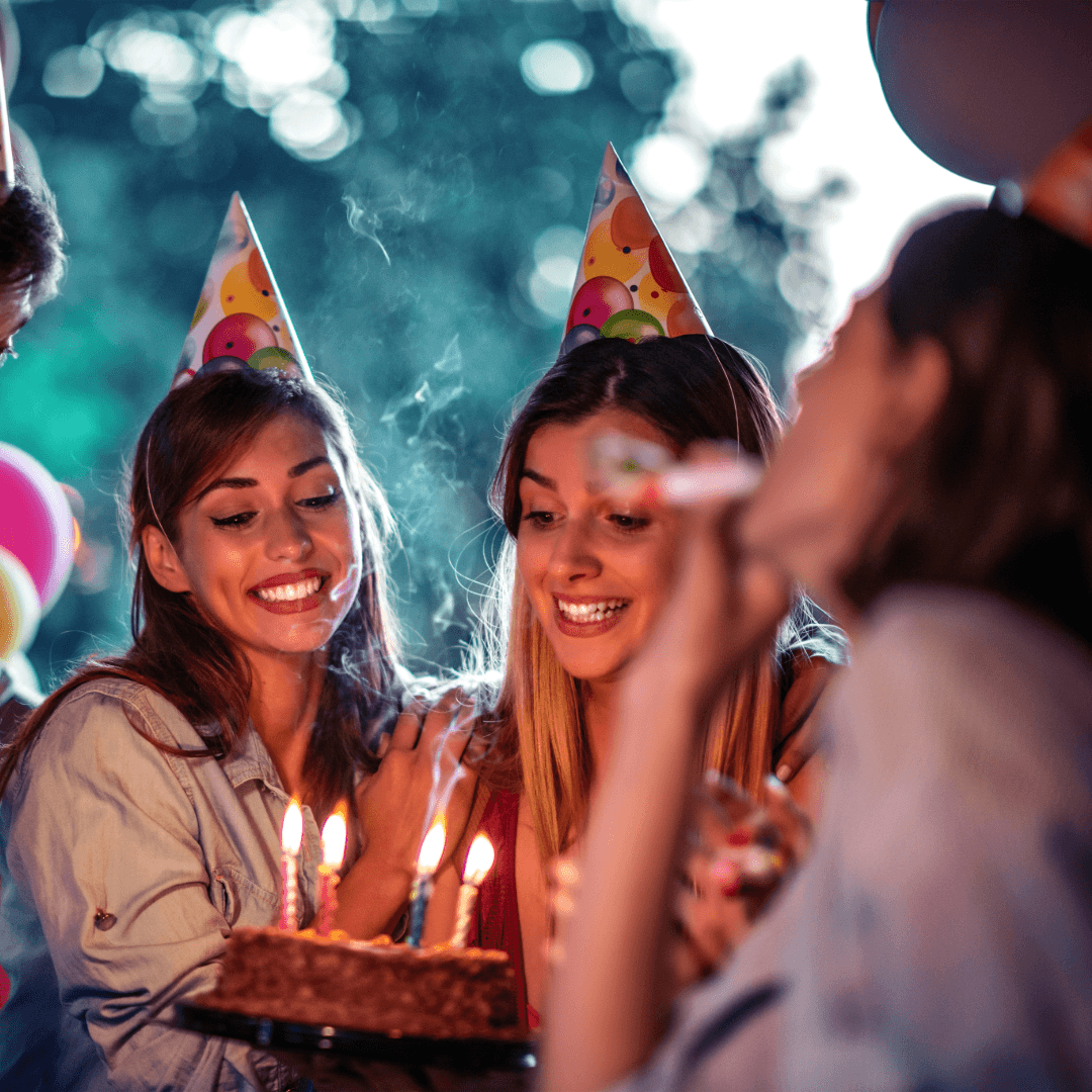 A group of friends celebrates with a birthday cake and party hats.