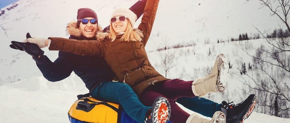 A joyful couple smiles and raises their arms while tubing down a snowy hill. A joyful couple smiles and raises their arms while tubing down a snowy hill.