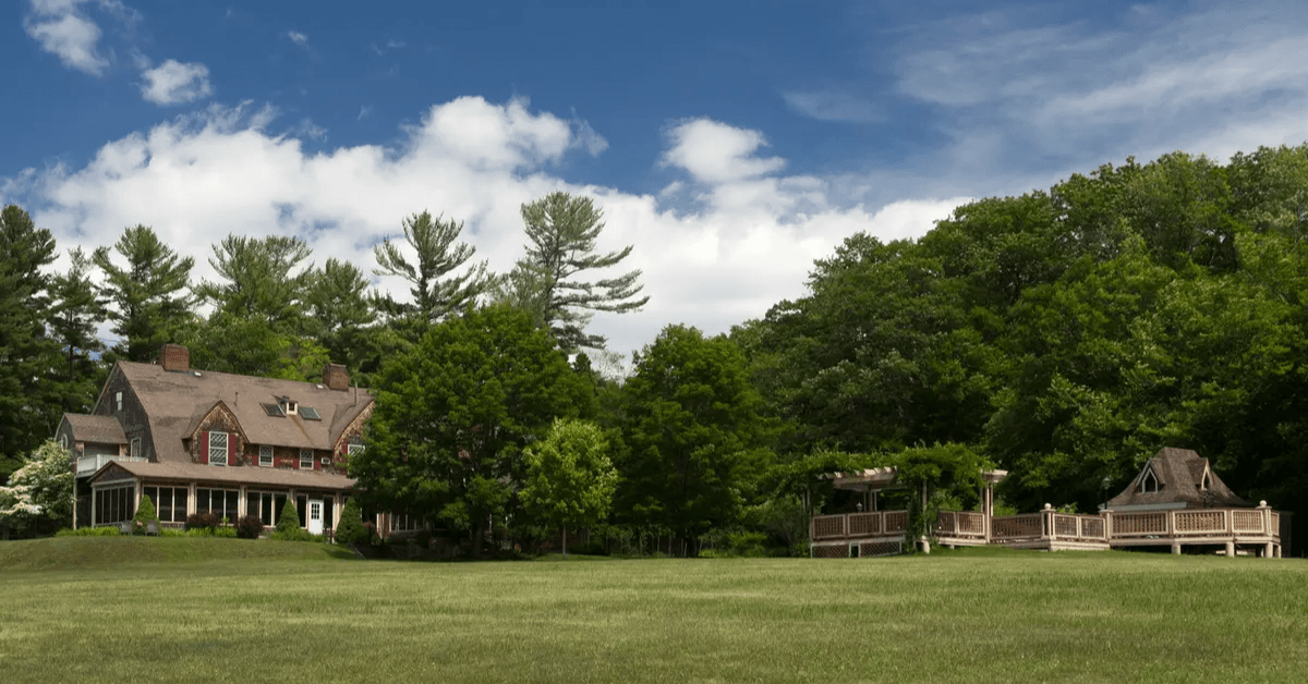 A large, well-maintained house surrounded by greenery and trees under a partly cloudy sky.
