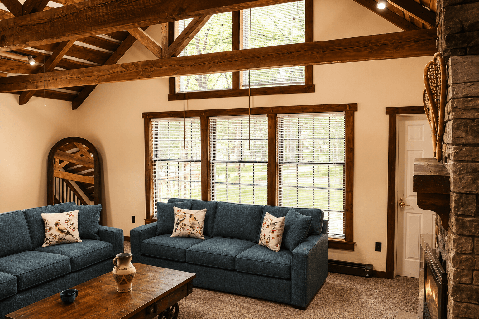 A cozy living room featuring two blue sofas, a wooden coffee table, and large windows with natural light.