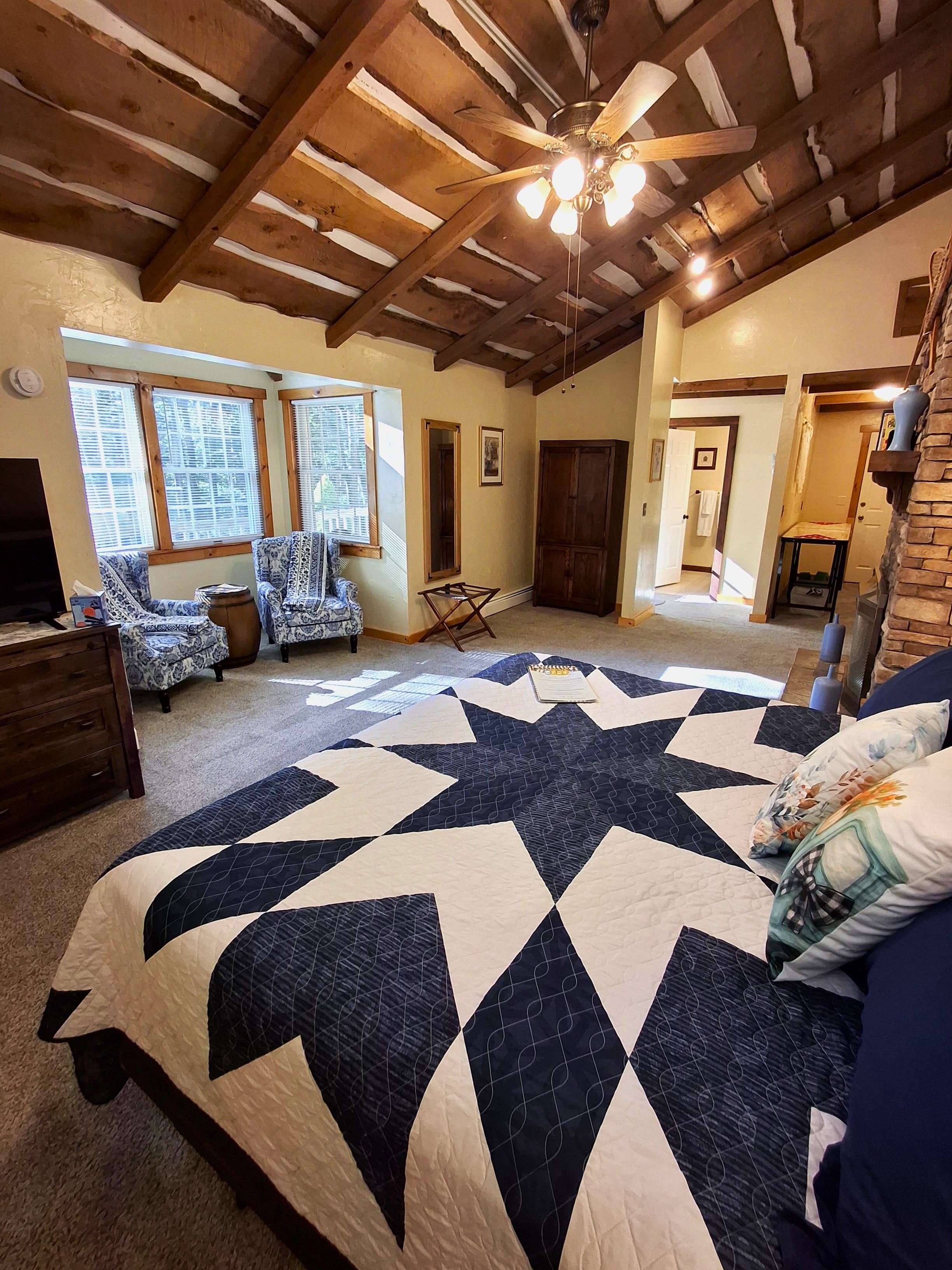Cozy bedroom with a star-patterned quilt, wooden ceiling beams, and seating area by the windows.