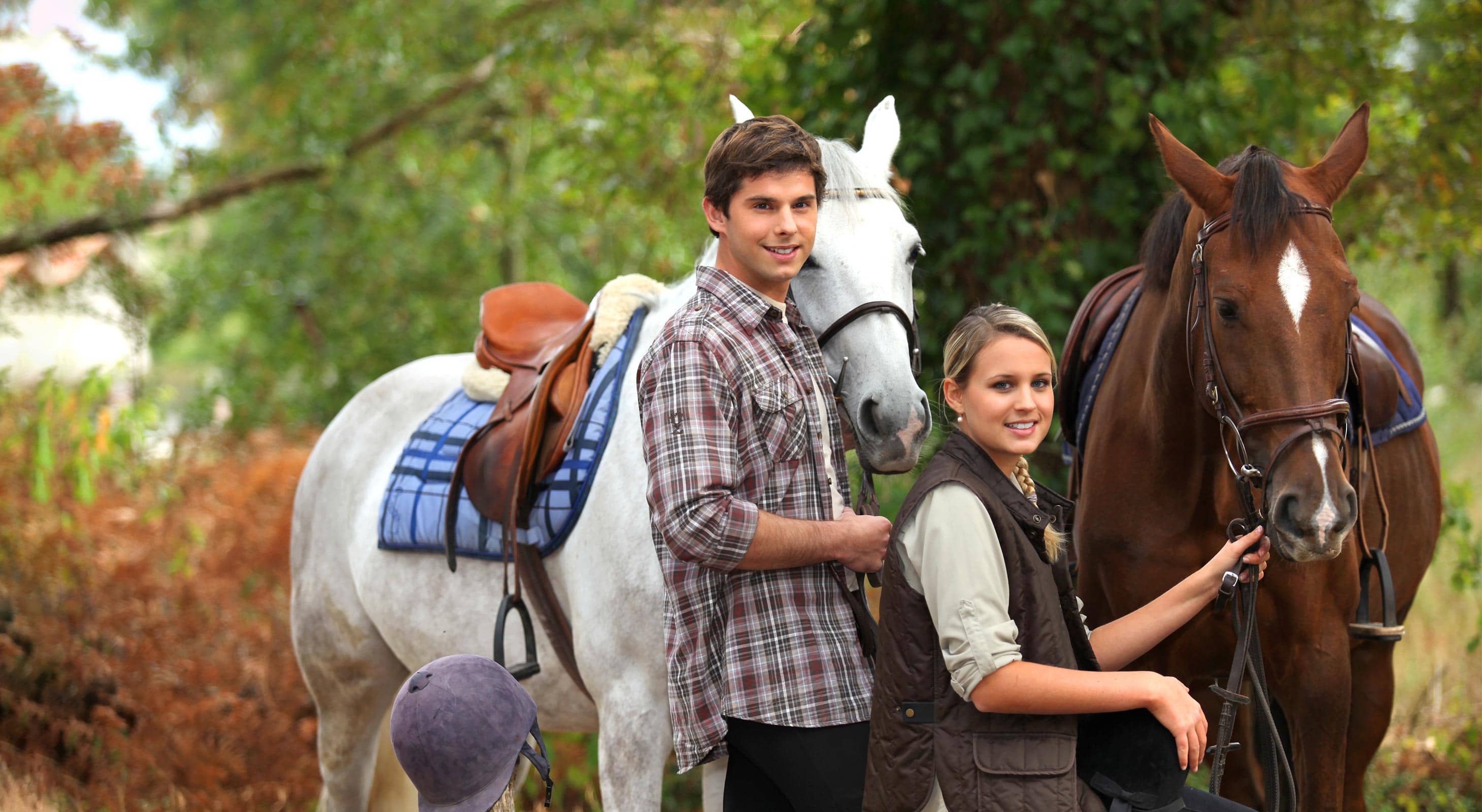 A young man and woman stand beside two horses in a serene outdoor setting. A young man and woman stand beside two horses in a serene outdoor setting.