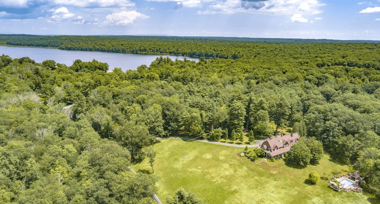 Aerial view of a spacious property with a house near a lake surrounded by dense trees.
