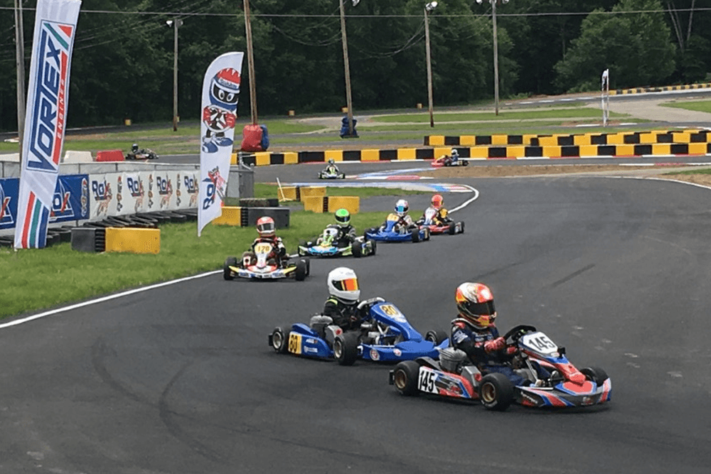 A group of go-karts racing on a track surrounded by greenery and banners.