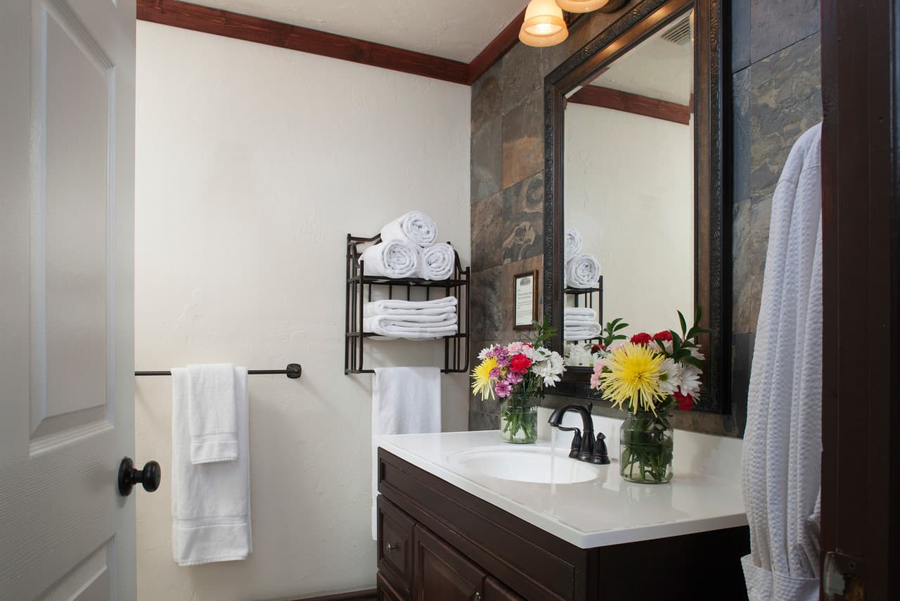 Bright bathroom featuring a dark vanity, stacked towels, and fresh floral arrangements.