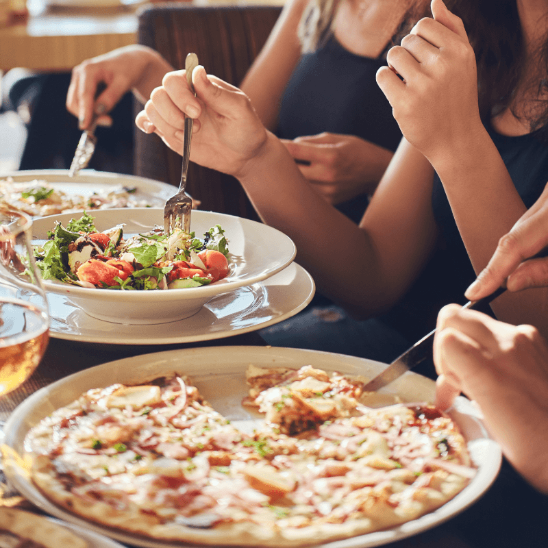 A group of people enjoying pizza and salad at a dining table.