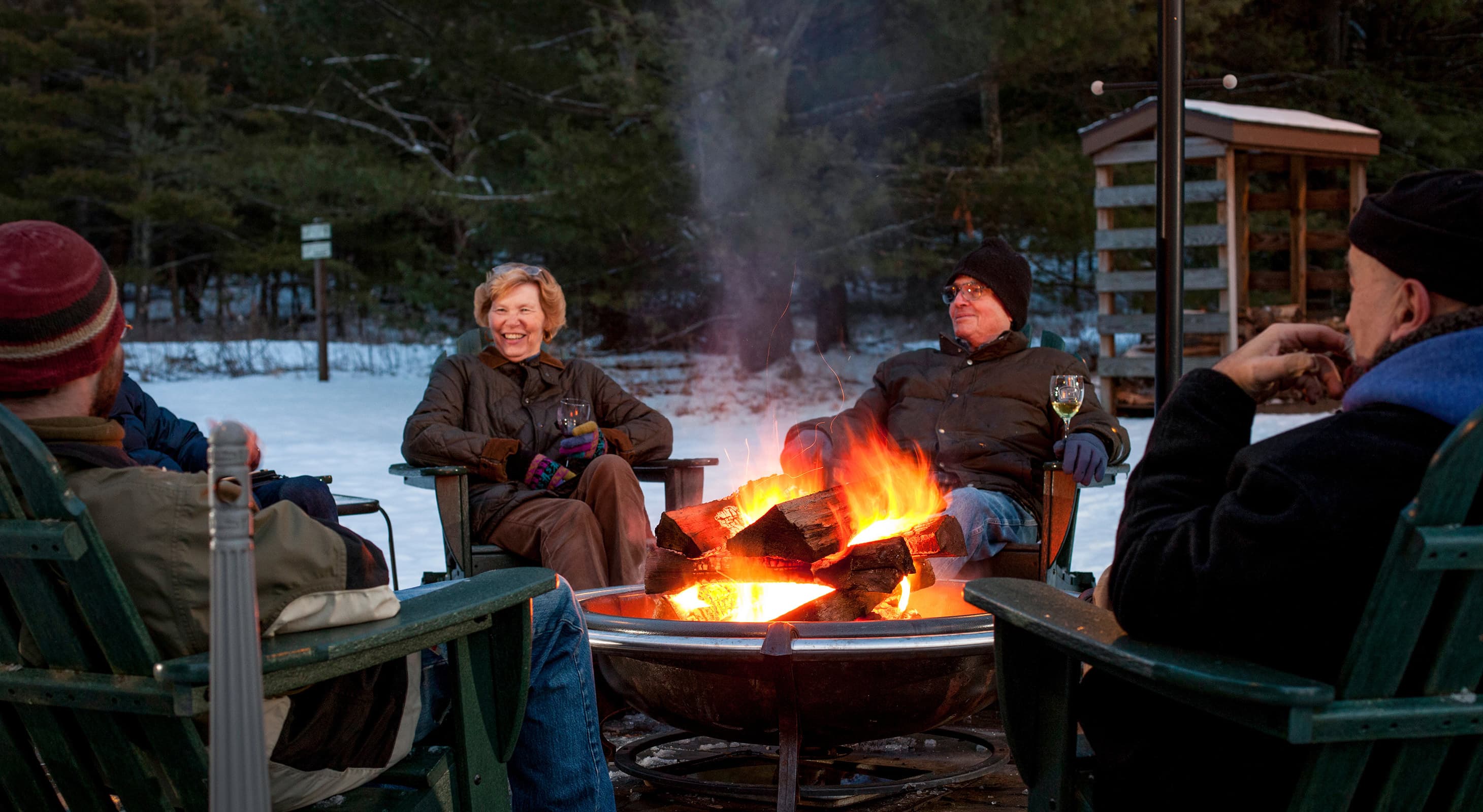 A group of people gathers around a cozy campfire in a snowy setting, enjoying each other's company.