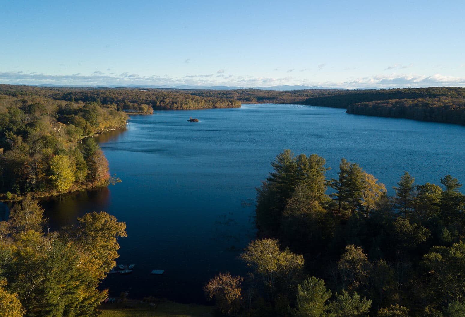 A tranquil lake surrounded by autumn-colored trees under a clear blue sky.