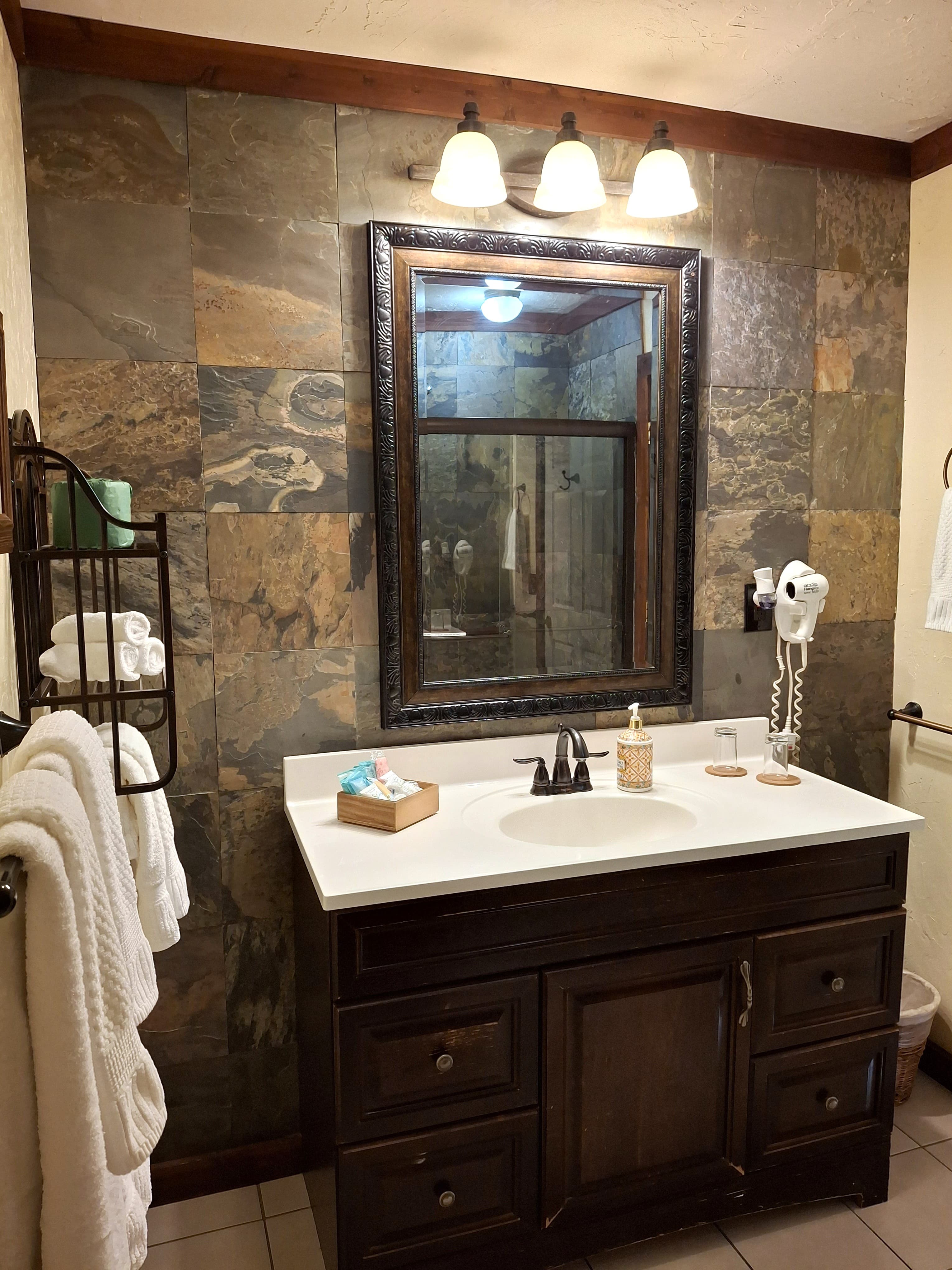 A modern bathroom featuring a stone accent wall, a mirrored cabinet, and a white sink with dark wood cabinetry.