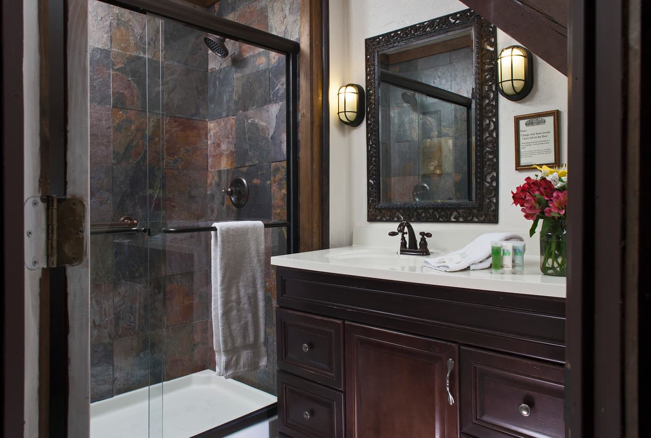 A stylish bathroom featuring a glass shower, dark wooden vanity, and decorative mirror.