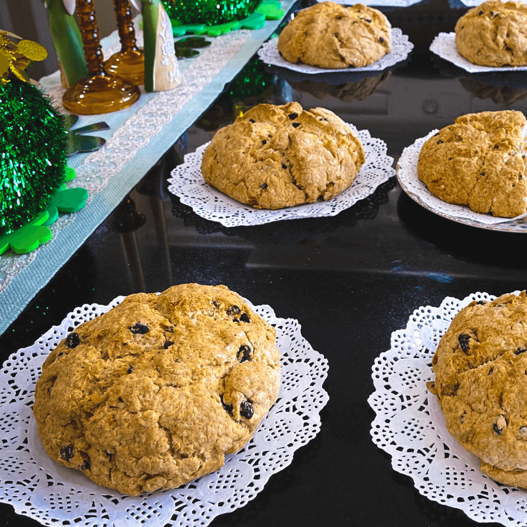 A selection of round, baked goods with raisins displayed on doilies on a glossy table.