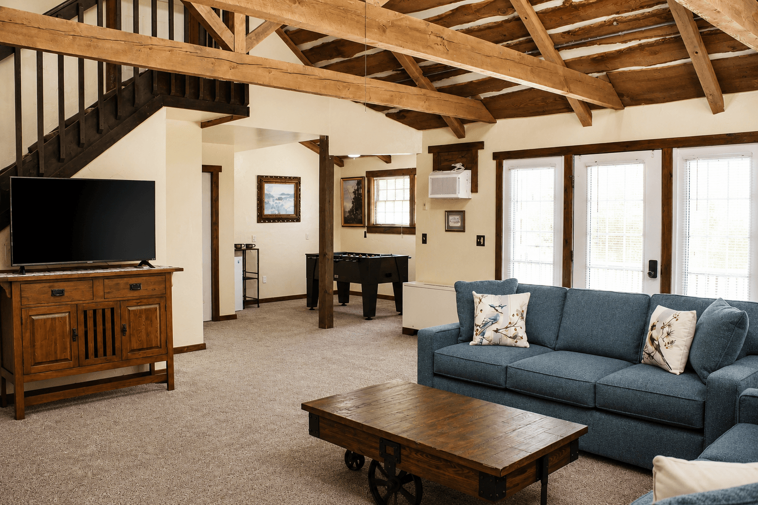 A cozy living room featuring a blue sofa, wooden coffee table, TV, and open wooden beams.