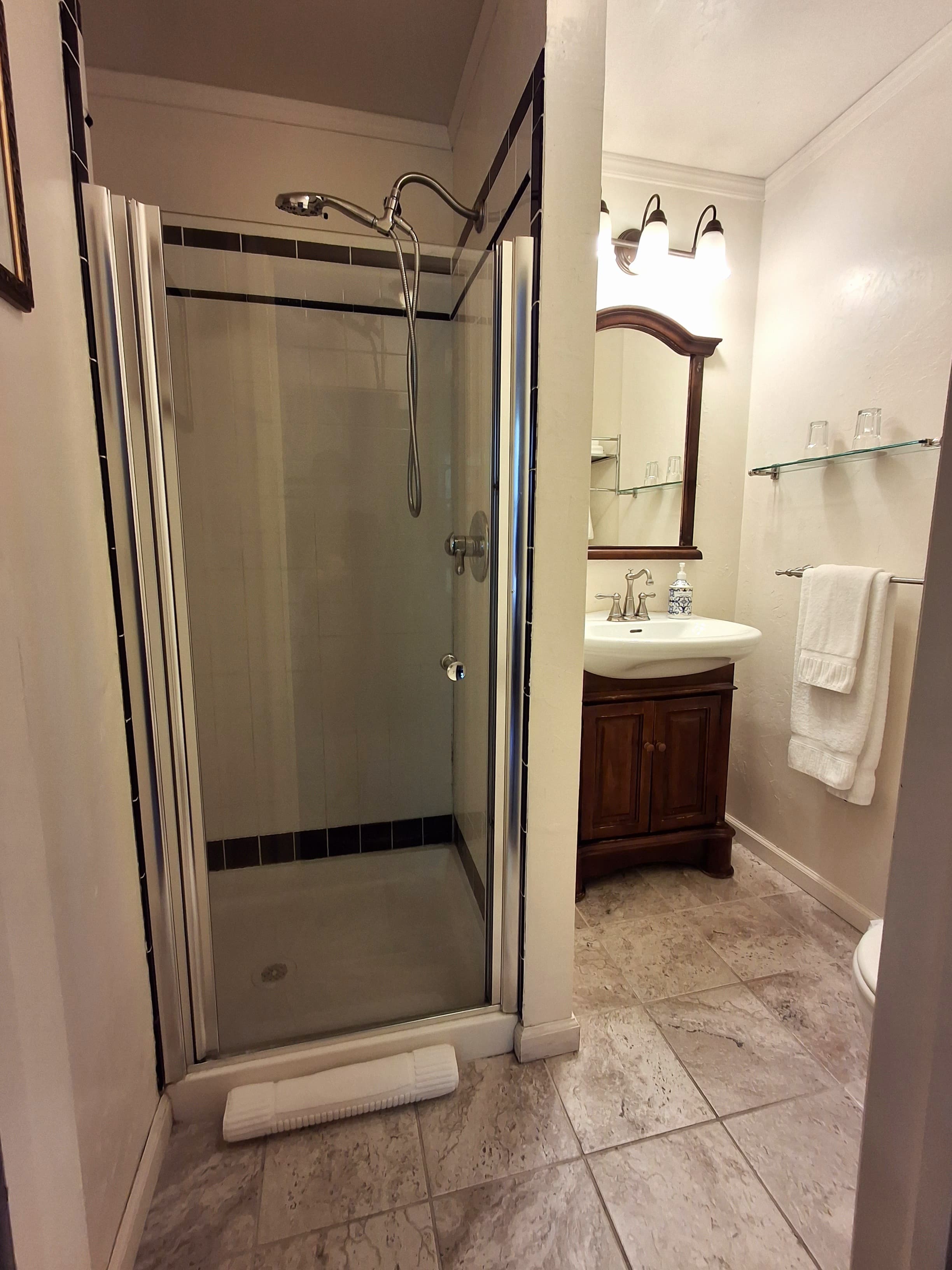 A small bathroom featuring a glass shower, a sink with a wooden cabinet, and decorative lighting.