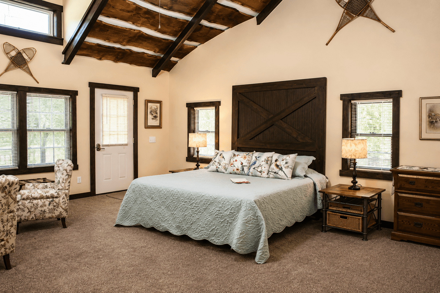 Cozy bedroom with a queen bed, floral accents, and rustic decor under a vaulted ceiling.