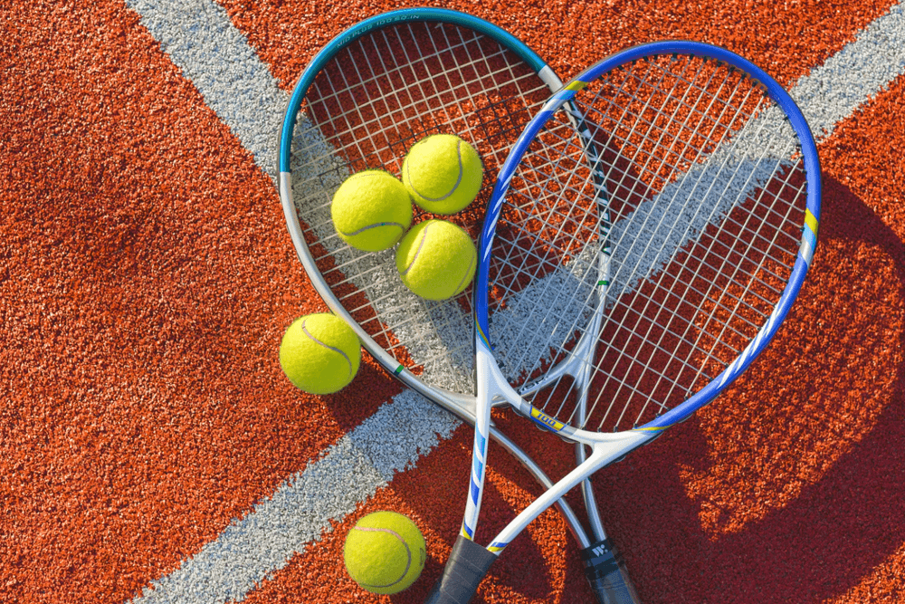 Two tennis rackets forming a heart shape with tennis balls on a clay court.