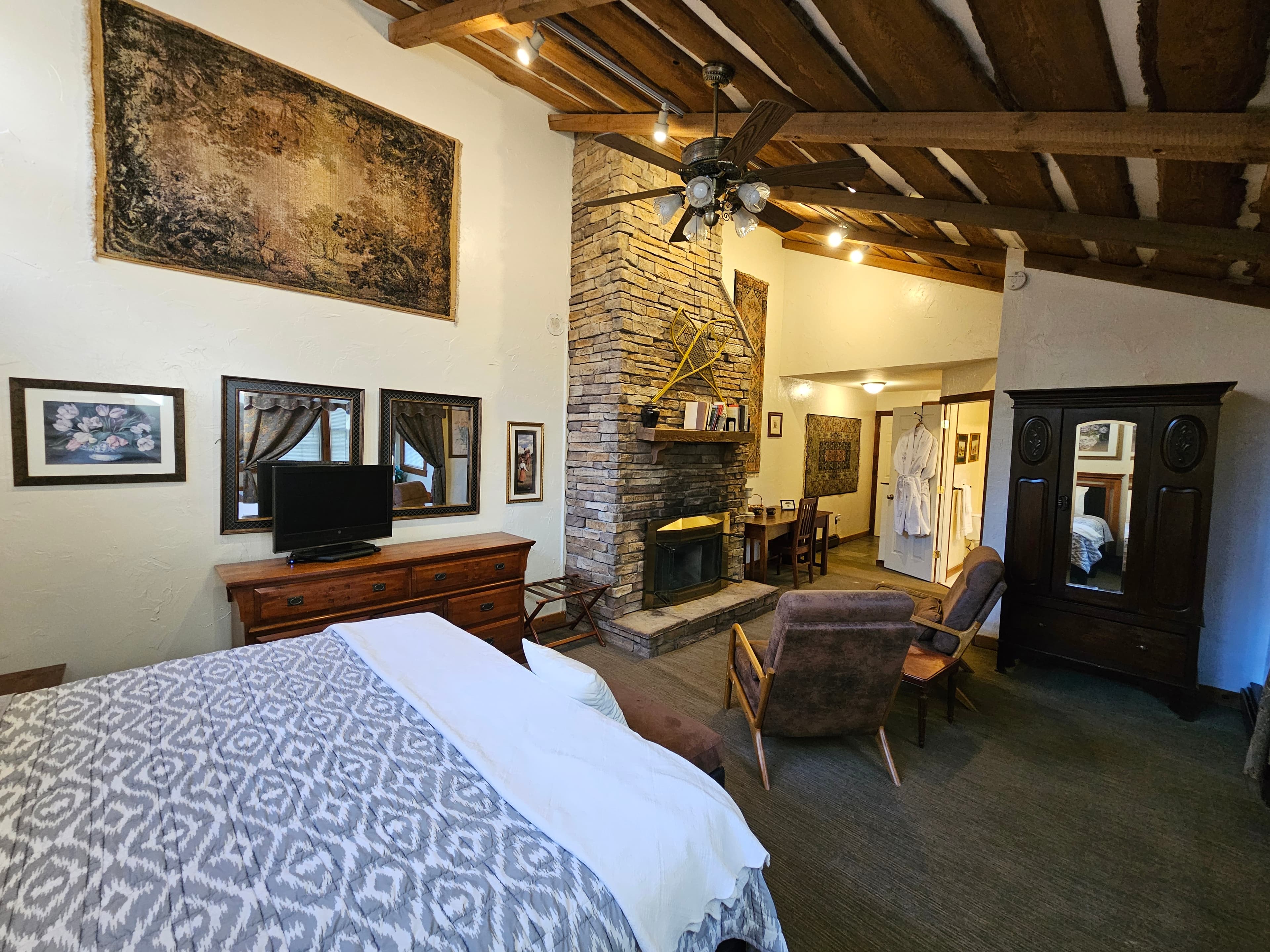 A cozy bedroom featuring a stone fireplace, wooden beams, and rustic furnishings.