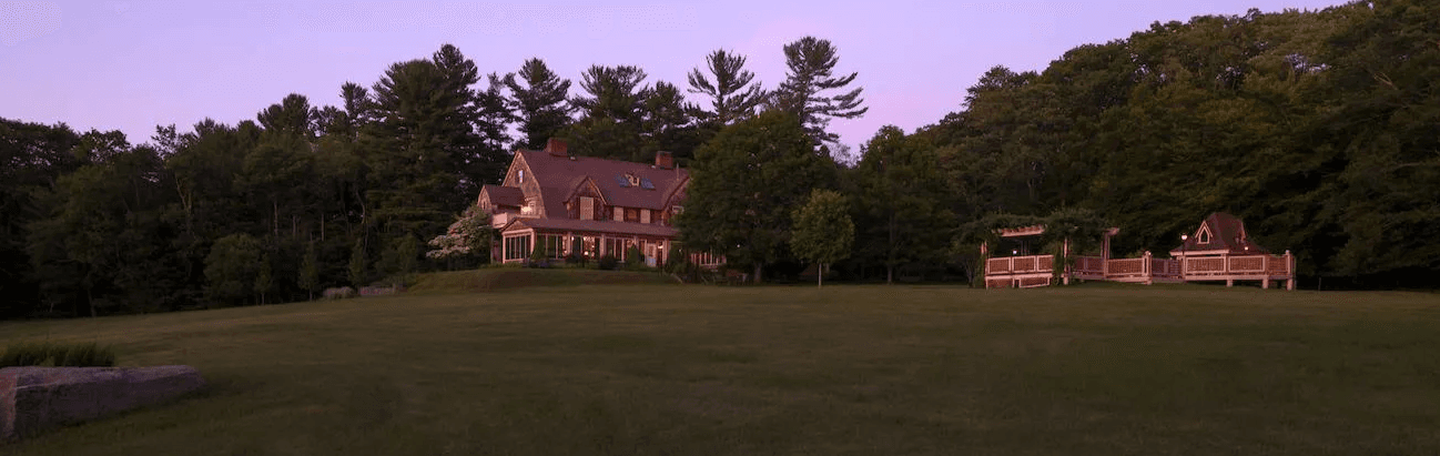 A large, elegant house surrounded by trees on a grassy landscape at twilight. A large, elegant house surrounded by trees on a grassy landscape at twilight.