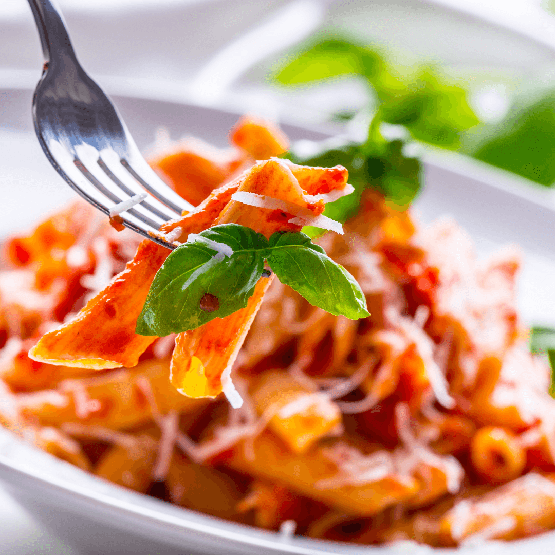 A fork holds pasta topped with basil and grated cheese.