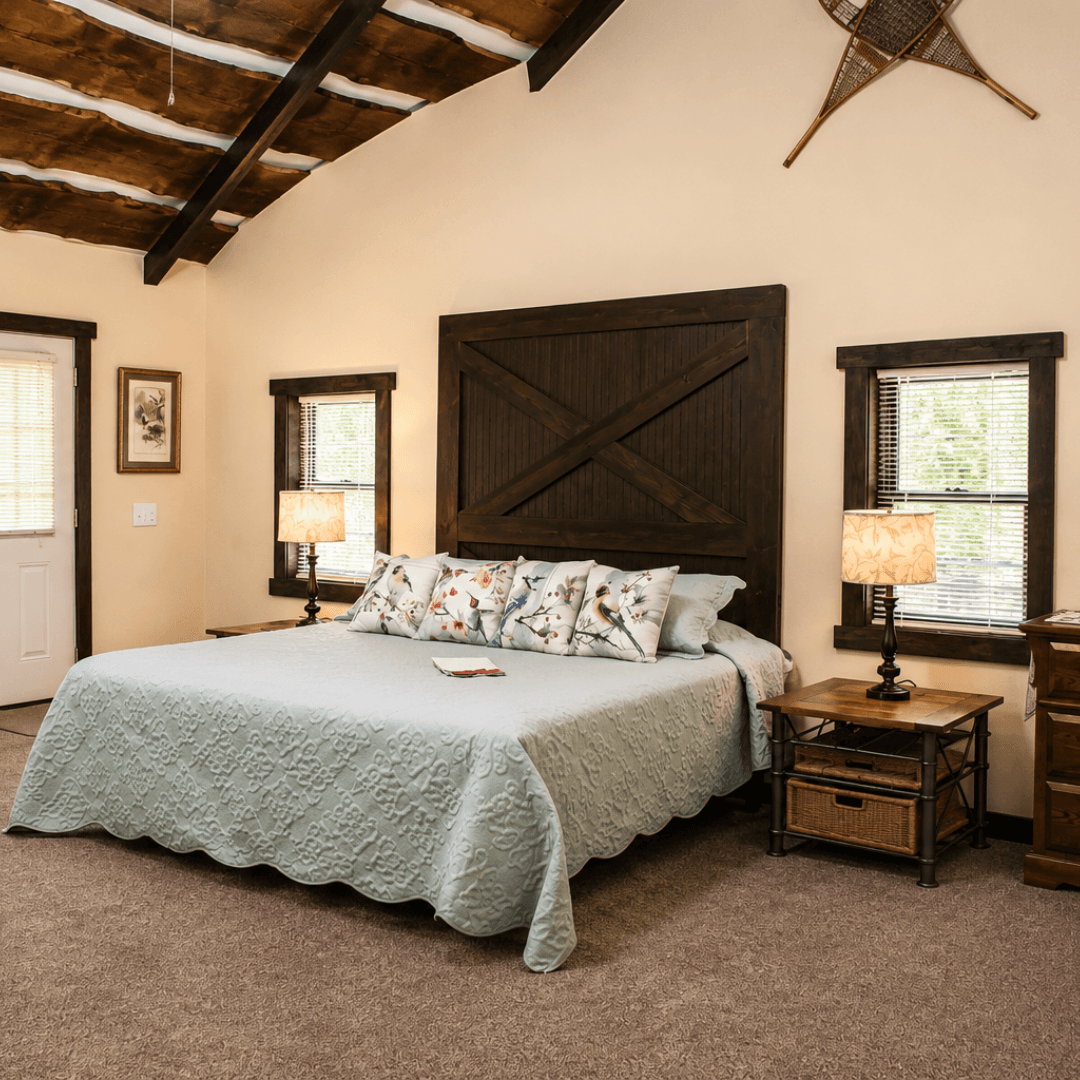 A cozy bedroom featuring a large bed with decorative pillows, two lamps, and rustic decor.
