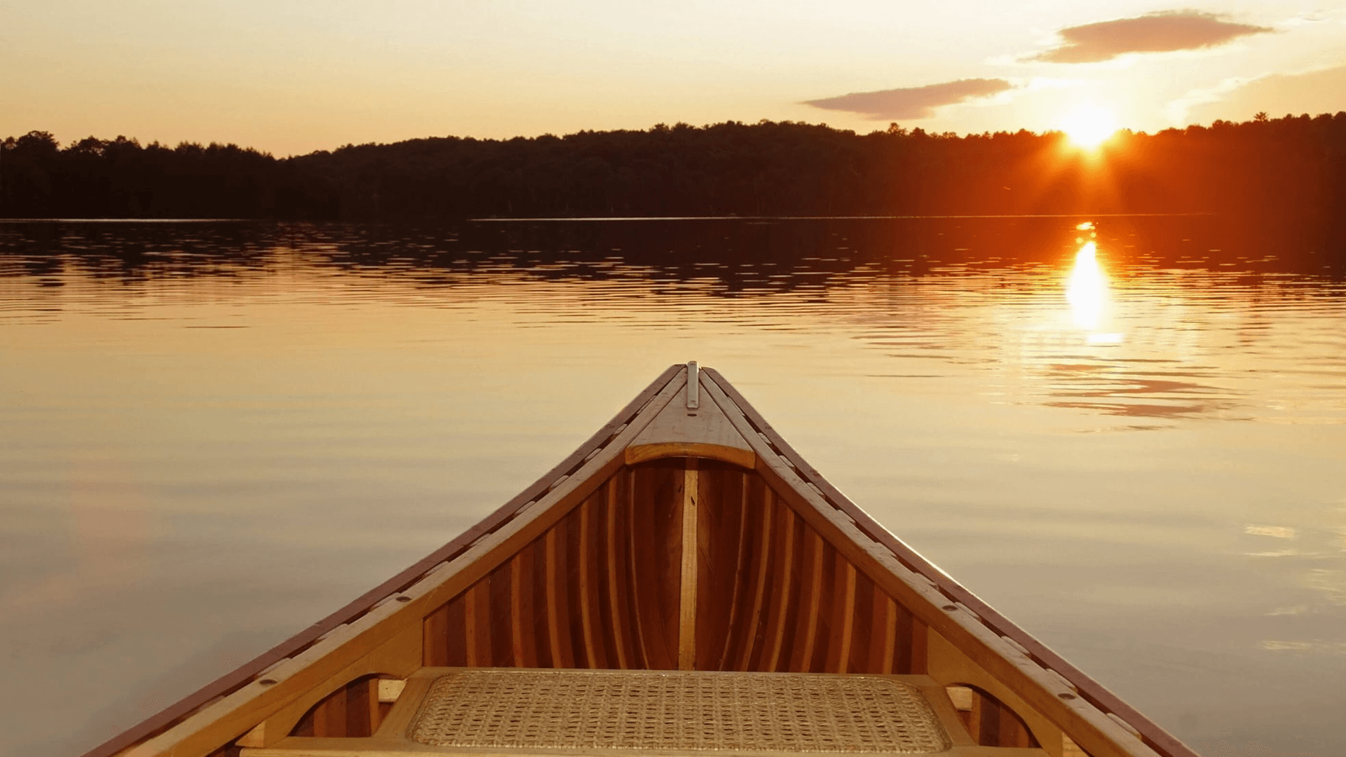 A wooden canoe faces a sunset over a calm lake.