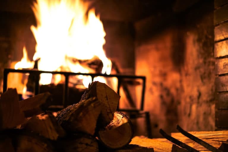 A warm fire burns brightly in a rustic fireplace, surrounded by stacked logs.
