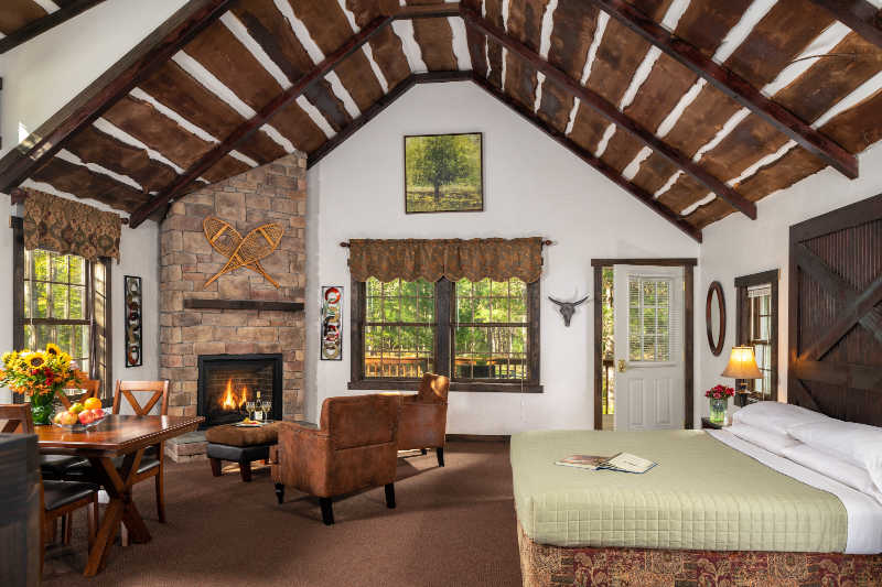 A cozy rustic bedroom with a stone fireplace, wooden beams, and a dining area.