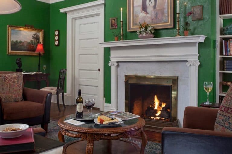 A cozy living room with a green wall, a fireplace, and comfortable seating, featuring a table with wine and snacks.