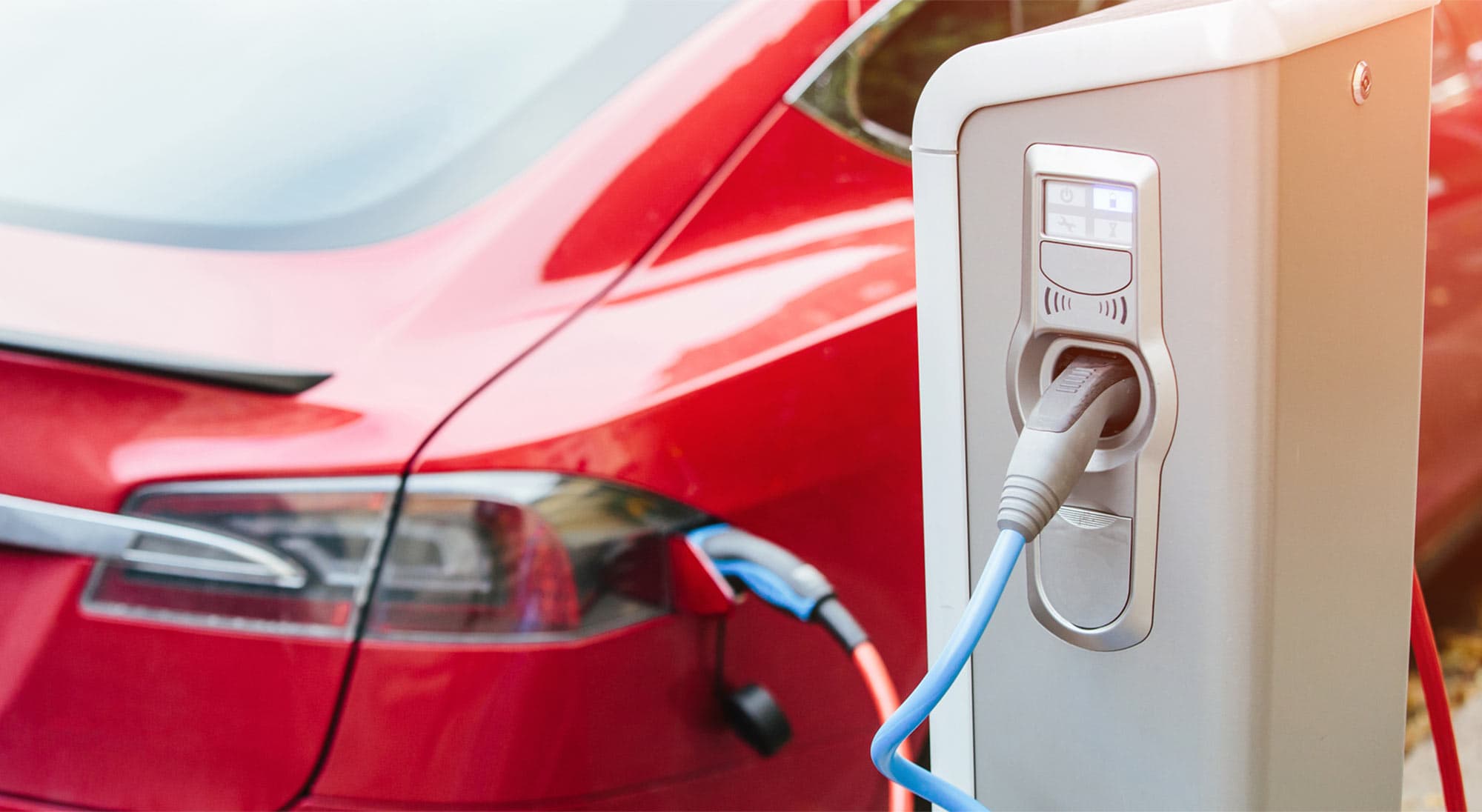 An electric vehicle charging station with a red car plugged in. An electric vehicle charging station with a red car plugged in.