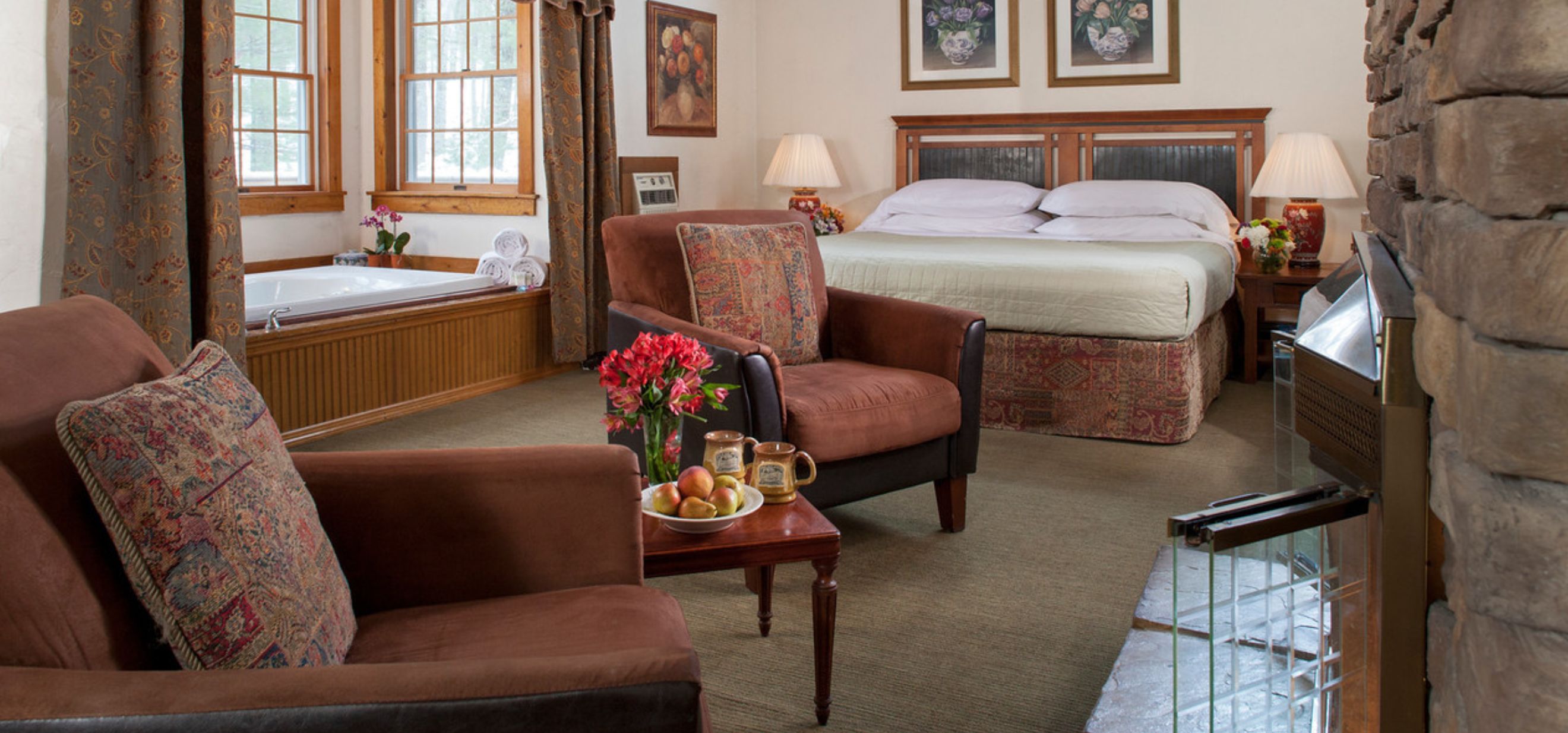A cozy bedroom with a bed, two chairs, side table, fireplace, and bathtub, creating a serene and inviting atmosphere.